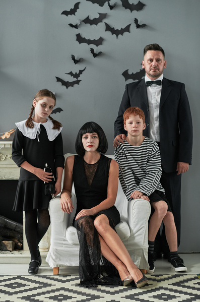 Parents and Their Children in Halloween Costumes on Background of Wall Decorated with Bats